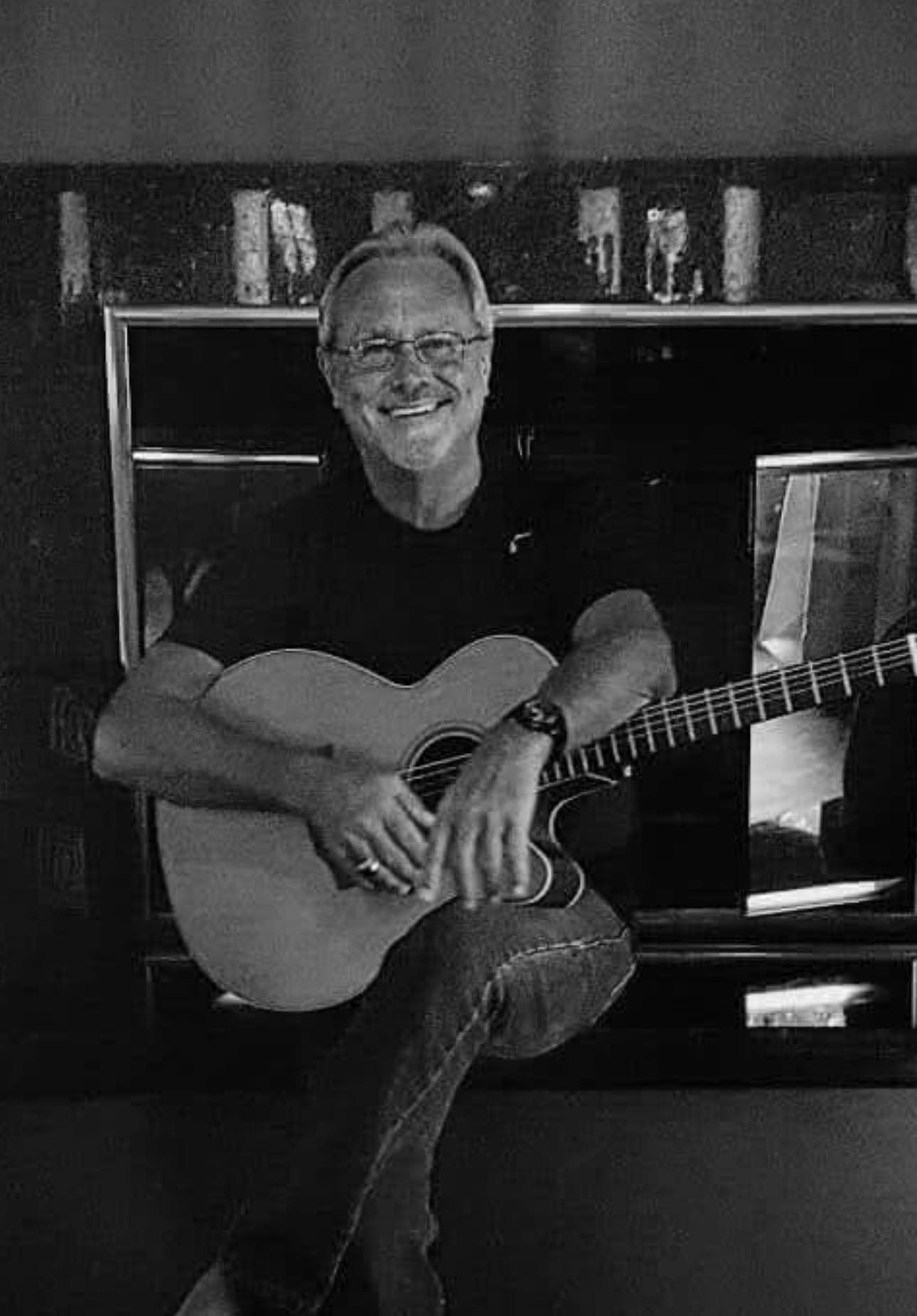 Denny Follis, musician; sits and smiles with his acoustic guitar